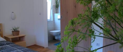 Et soveværelse med seng, et natbord med en plante og udsigt til badeværelset.