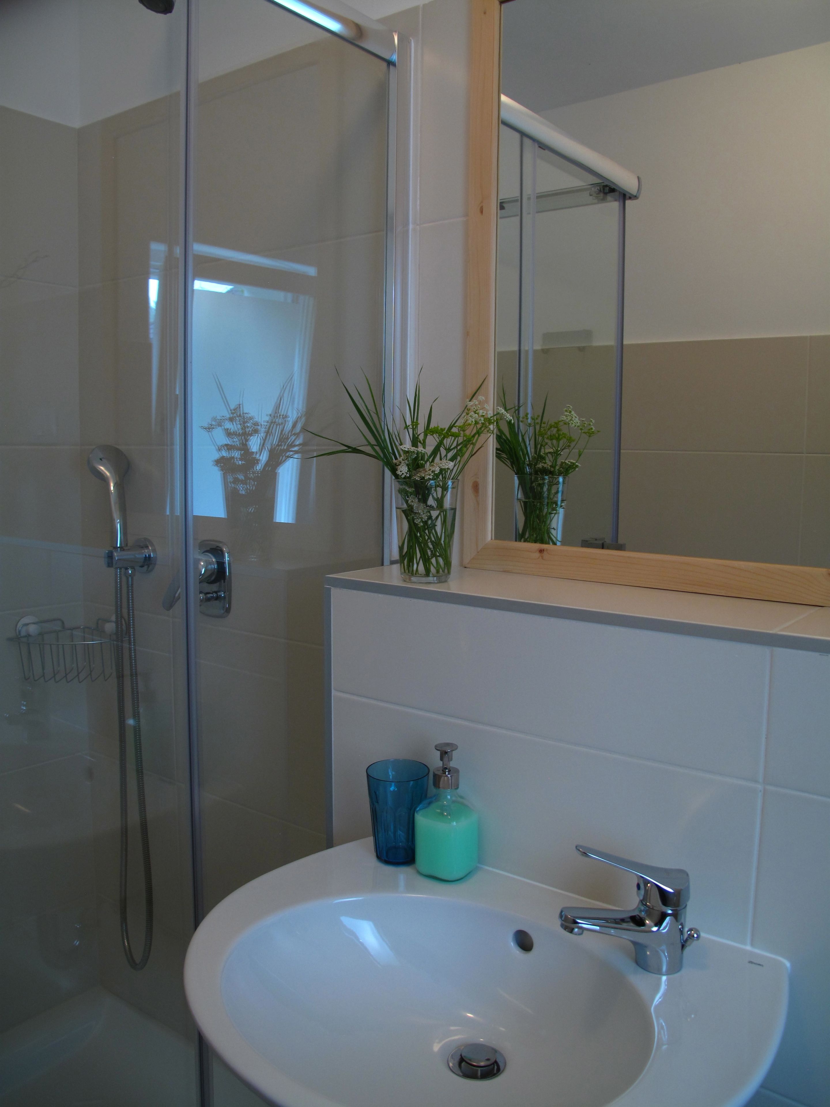 Un bagno con cabina doccia in vetro, un lavandino bianco con rubinetteria cromata e uno specchio sopra il lavandino.