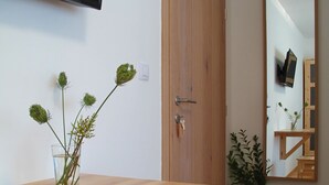 A room with a wooden desk, a small wooden stool, a potted plant, a mirror, and a television mounted on the wall. - Guesthouse Bor (Plitvicka Jezera)