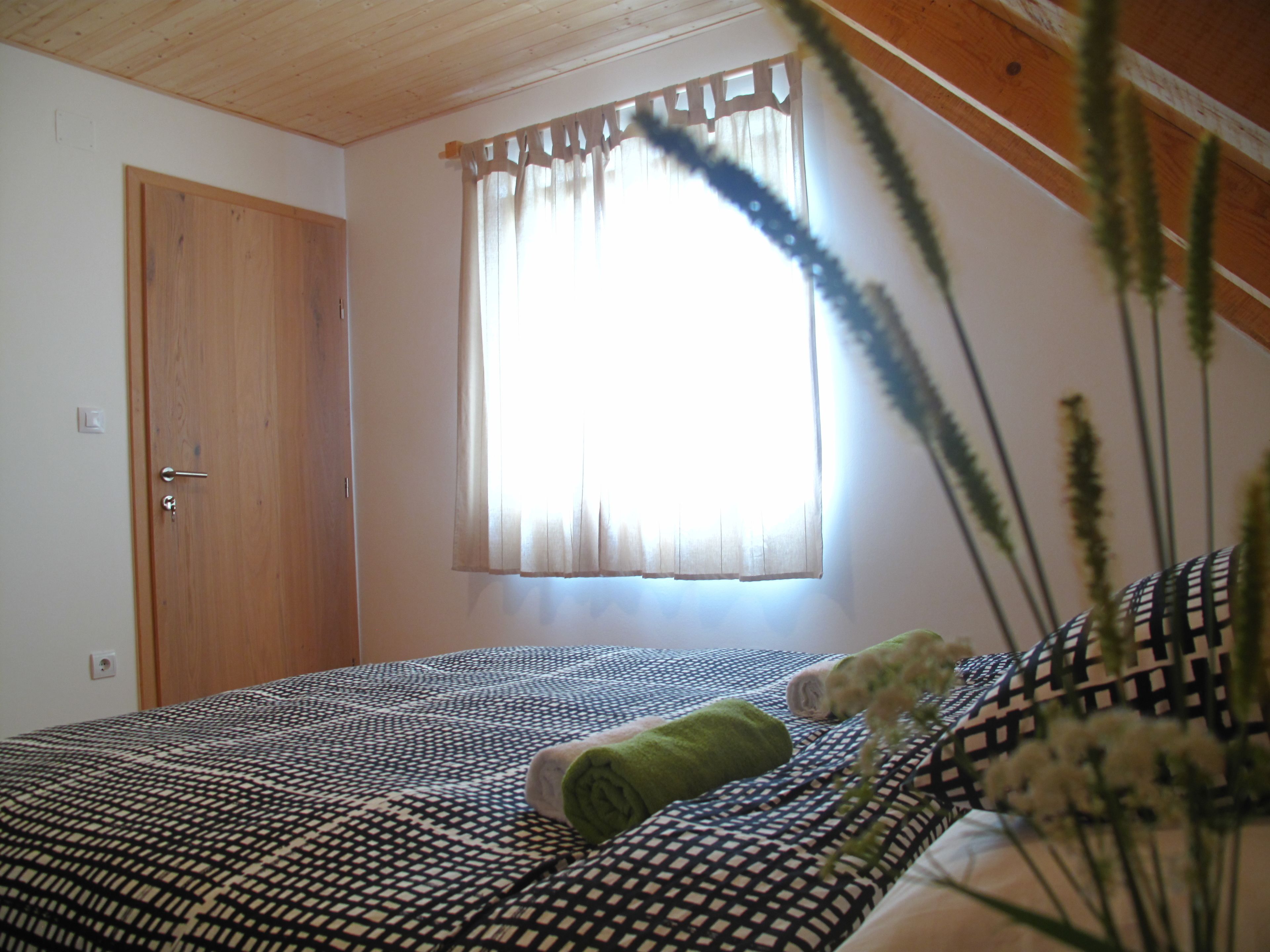 Un dormitorio con techo de madera, una ventana con cortinas, una cama con ropa de cama estampada y una puerta.