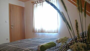 Un dormitorio con techo de madera, una ventana con cortinas, una cama con ropa de cama estampada y una puerta.