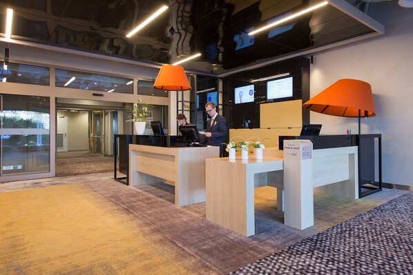 Zona de recepción con escritorio, dos lámparas naranjas, una computadora y un letrero que dice 'Fast Check-Out'.