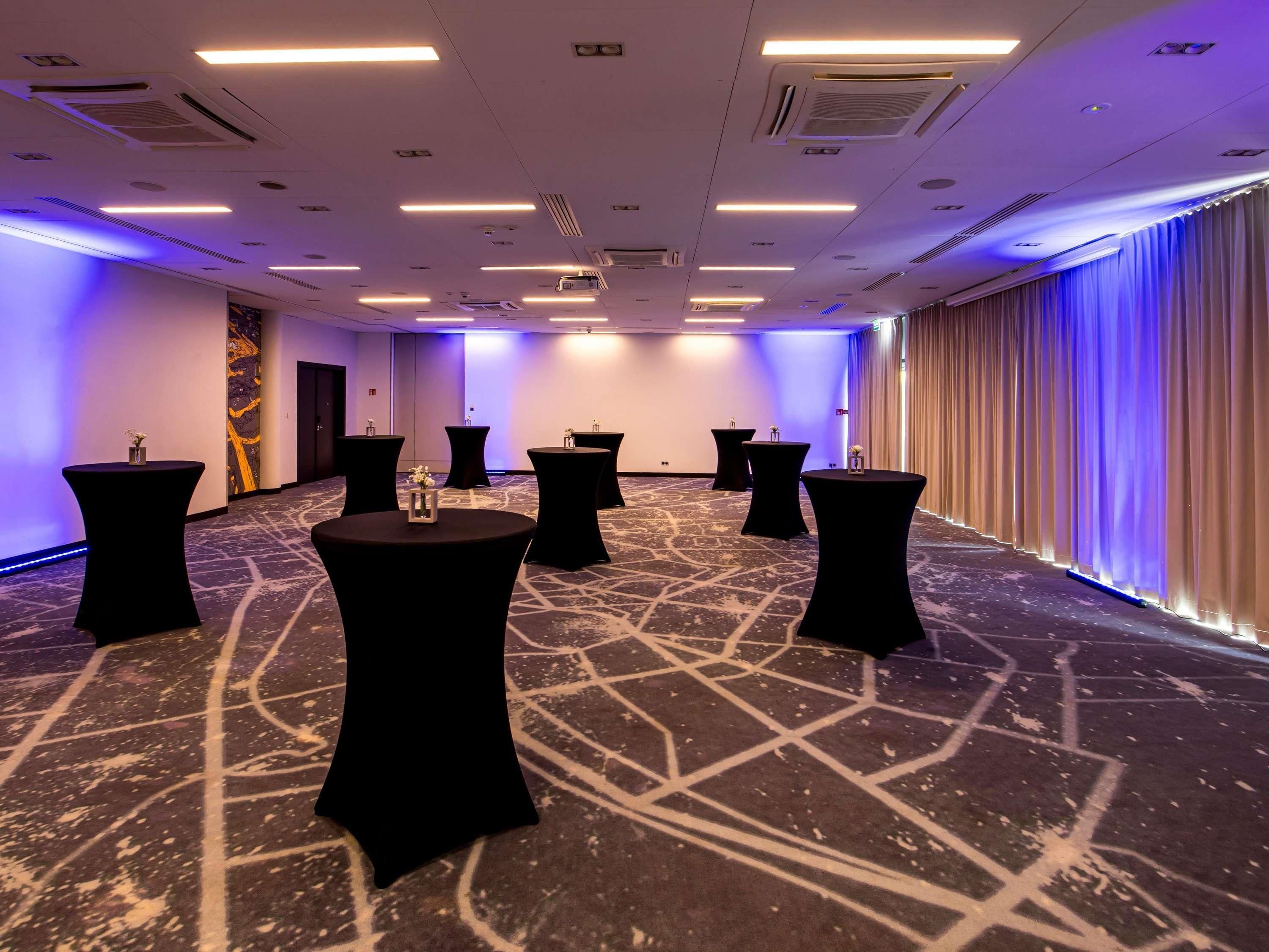 Une salle de conférence dotée de plusieurs tables, d’un tapis à motifs et d’une grande fenêtre avec des rideaux.