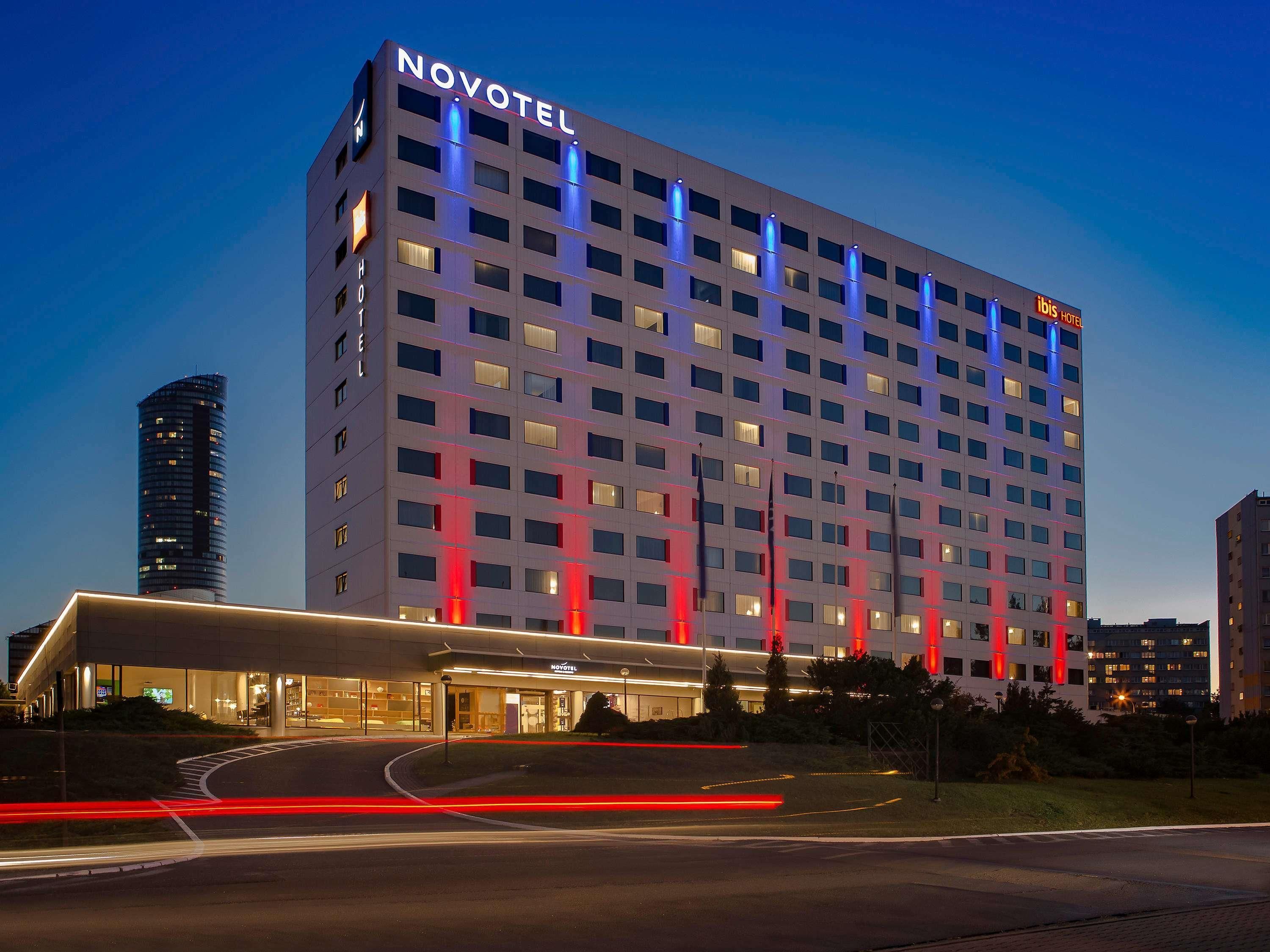 Un hôtel à plusieurs étages, reconnaissable à son grand panneau « NOVOTEL », doté d’une architecture moderne et d’un hall d’entrée bien éclairé.