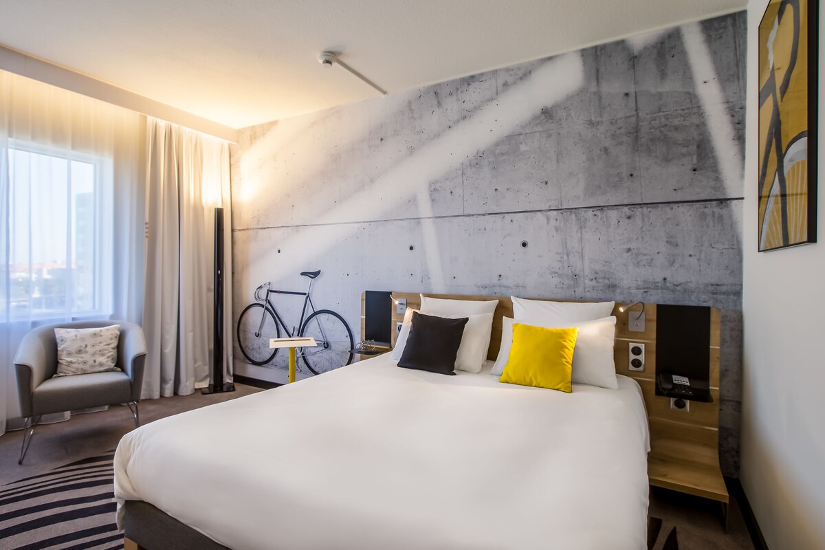 Una habitación de hotel moderna con una cama grande, una bicicleta y vistas a la ciudad.