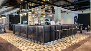 Zona de bar con mostrador, taburetes y estantes llenos de botellas.