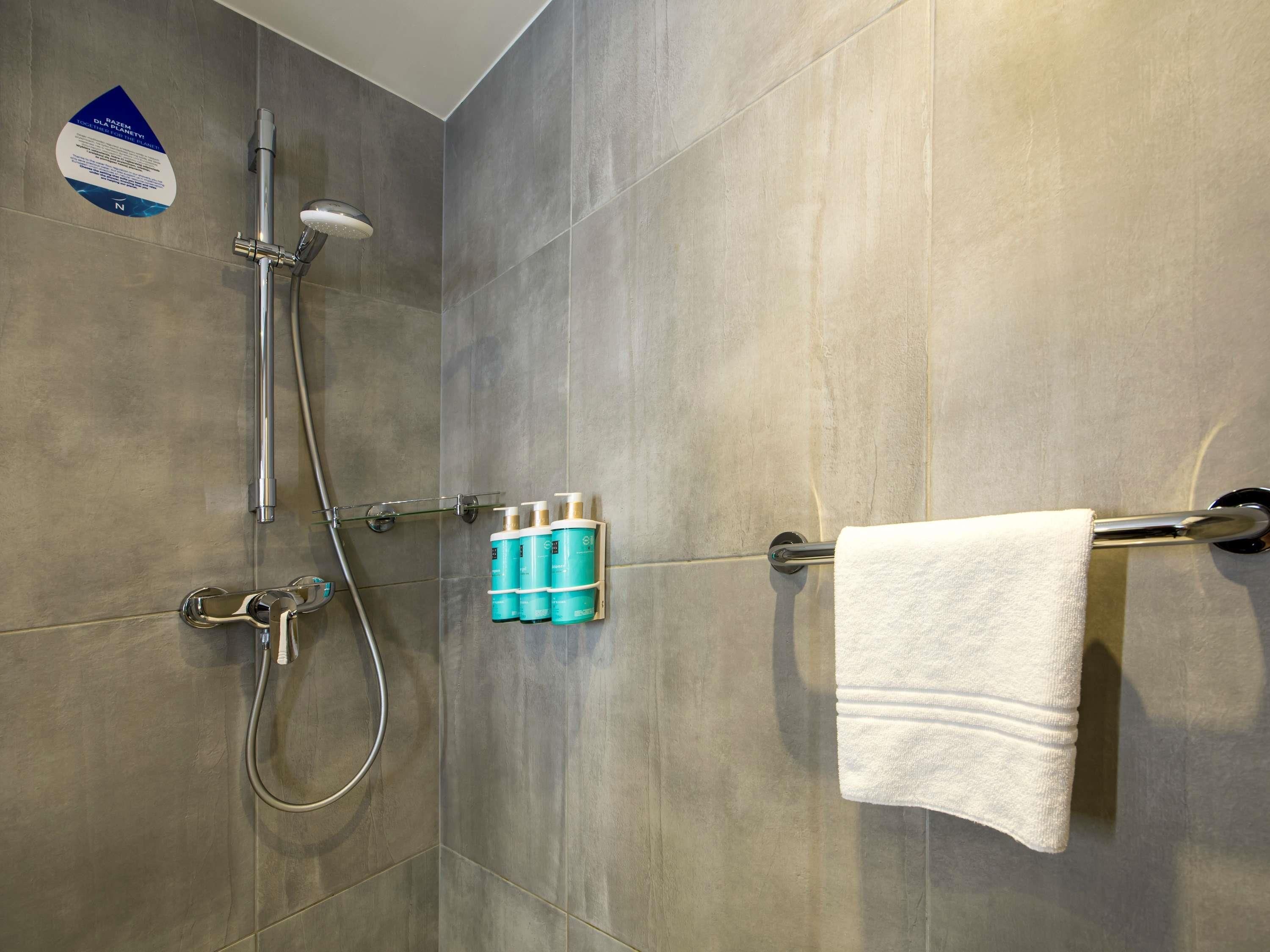 A shower area with a glass door, a towel rack with a white towel, and a set of toiletries.
