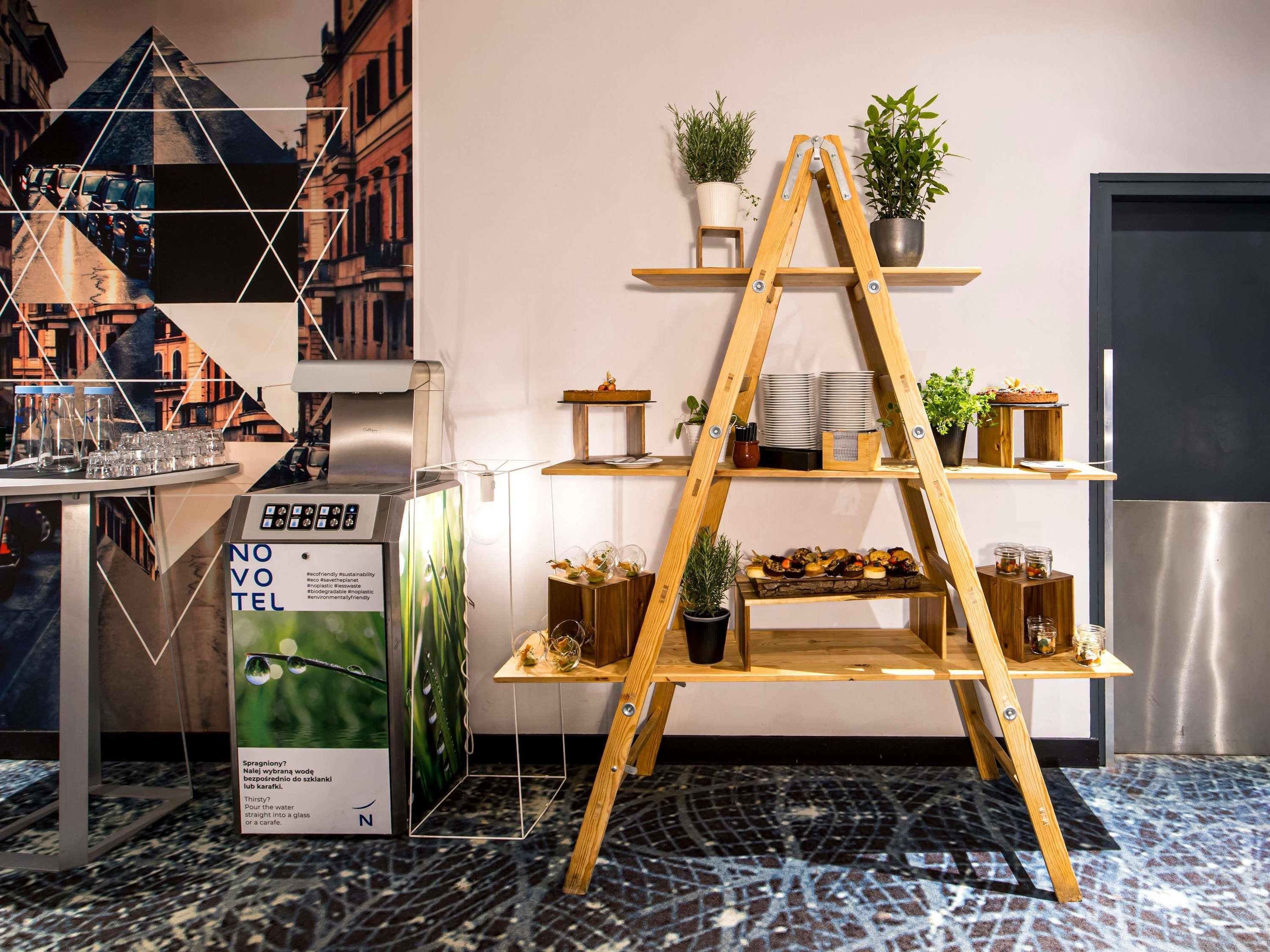A modern hotel interior with a kitchen area, a wooden ladder shelf, and a refrigerator.