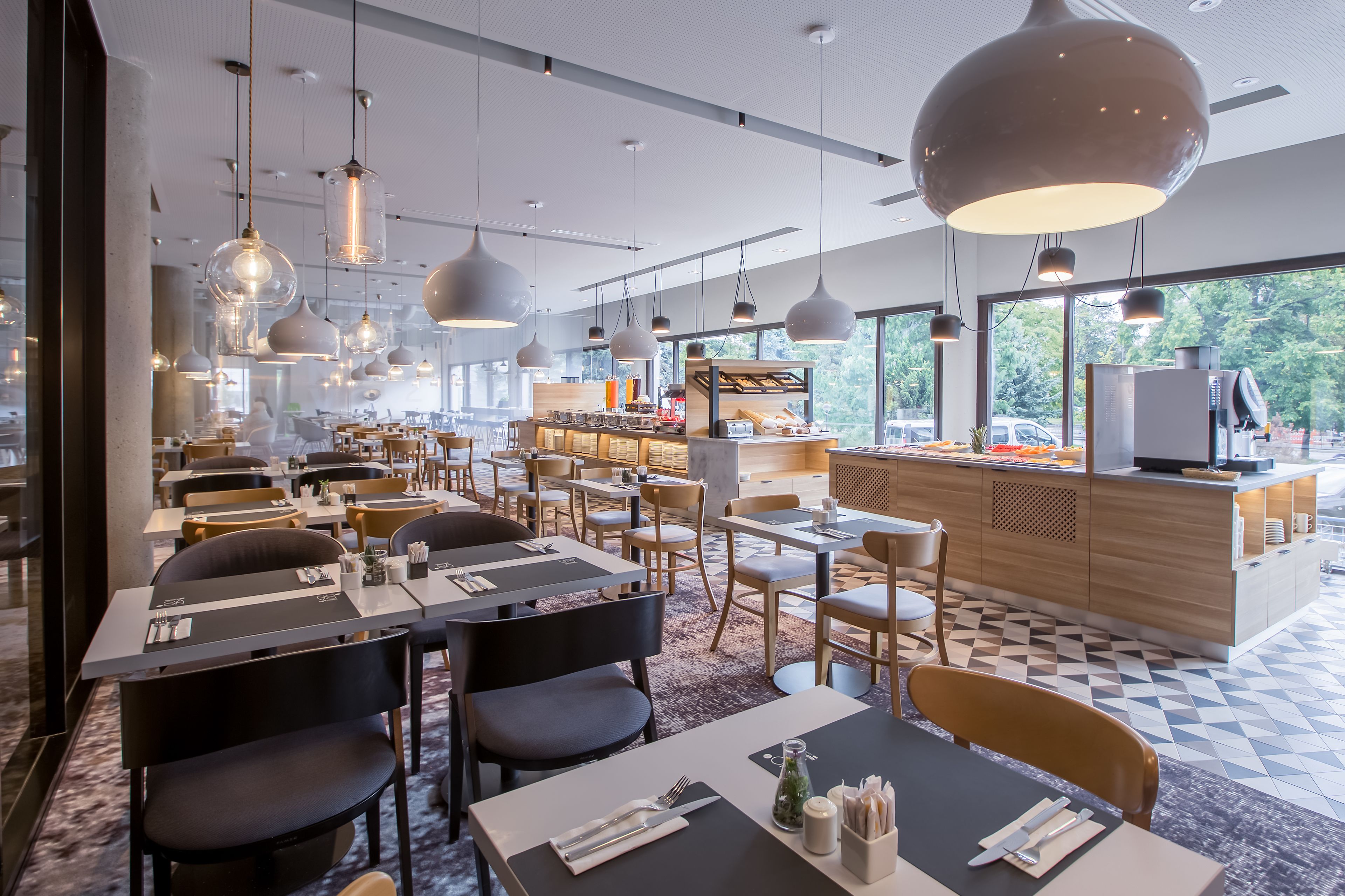 A modern restaurant with multiple dining areas, pendant lighting, and a view of the outdoors.
