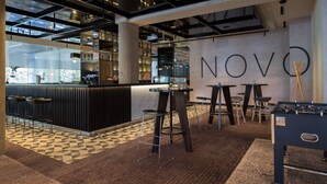 Un área de bar moderna con una mesa de fútbol, taburetes y un mostrador con estantes llenos de botellas.