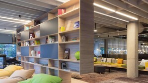 A modern interior with a wooden bookshelf, a seating area with cushions, and a view of the outside. - Novotel Wroclaw Centrum (Wroclaw)