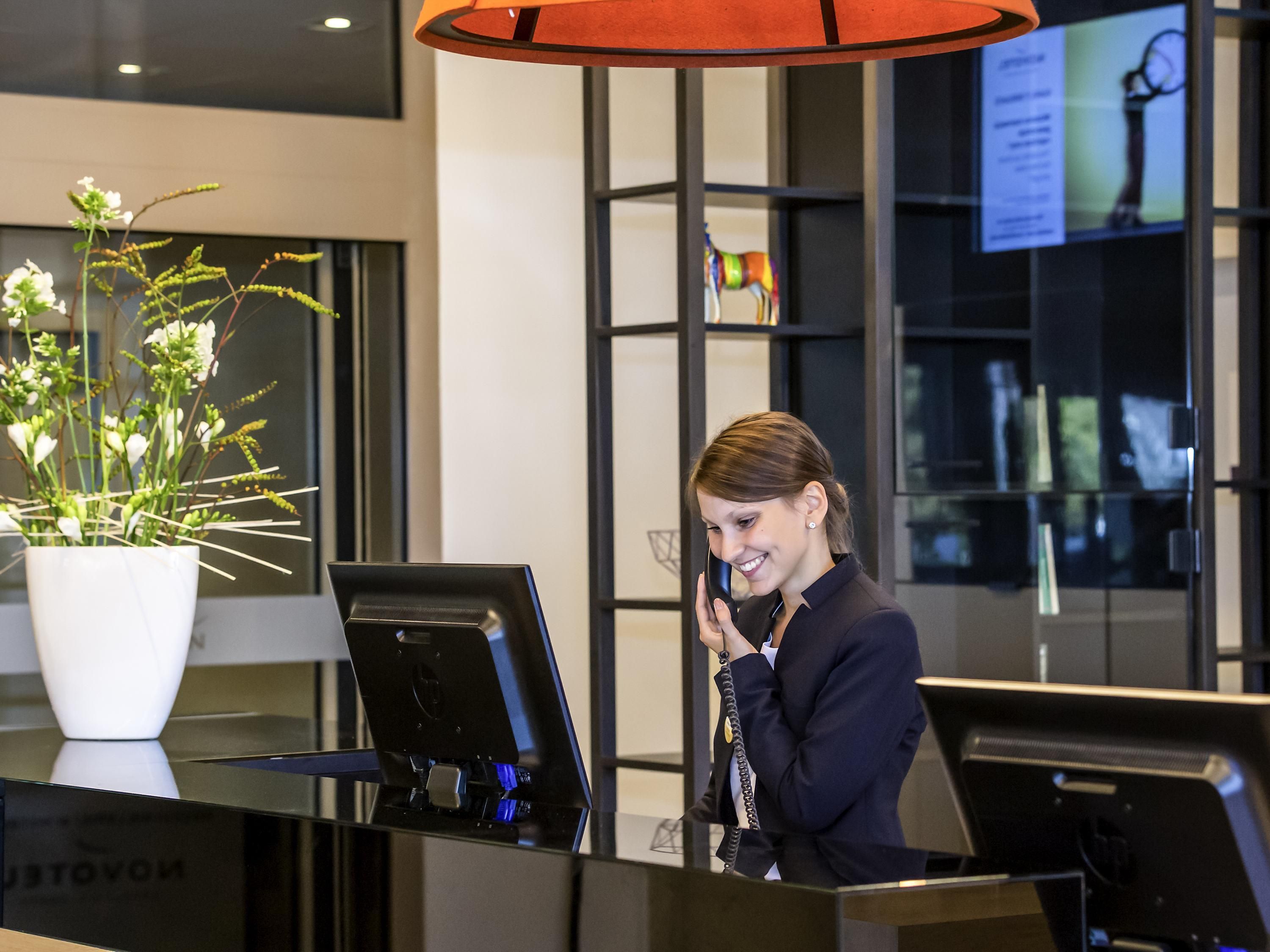 Un mostrador de recepción con una computadora portátil, una planta en maceta y un amplio ventanal con vistas al interior.