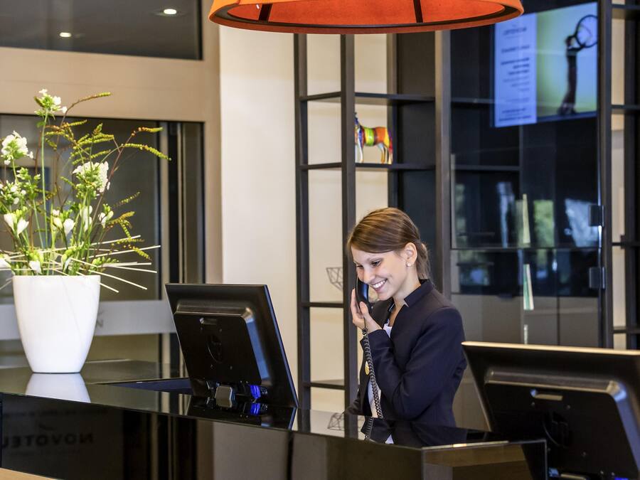 Un mostrador de recepción con una computadora portátil, una planta en maceta y un amplio ventanal con vistas al interior.