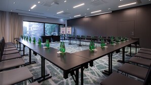 Un salón de conferencias con mesas largas, sillas y botellas verdes en cada una.