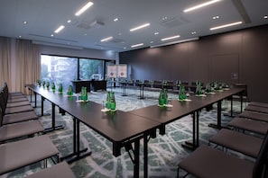 Un salón de conferencias con mesas largas, sillas y botellas verdes en cada una.