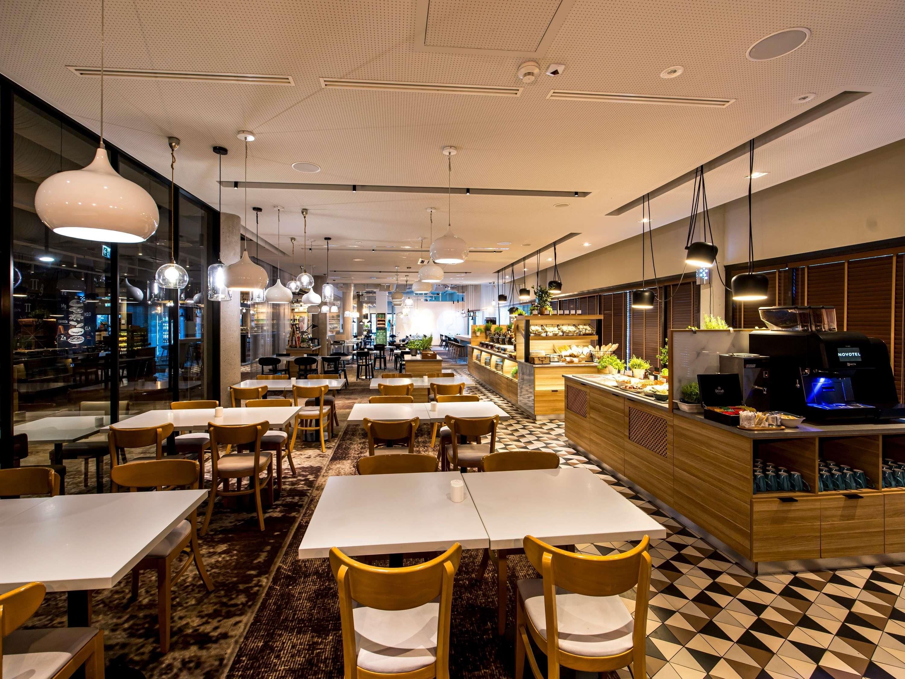 En modern restauranginteriör med flera matbord och stolar, en bardisk med en kaffemaskin och ett mönstrat golv.