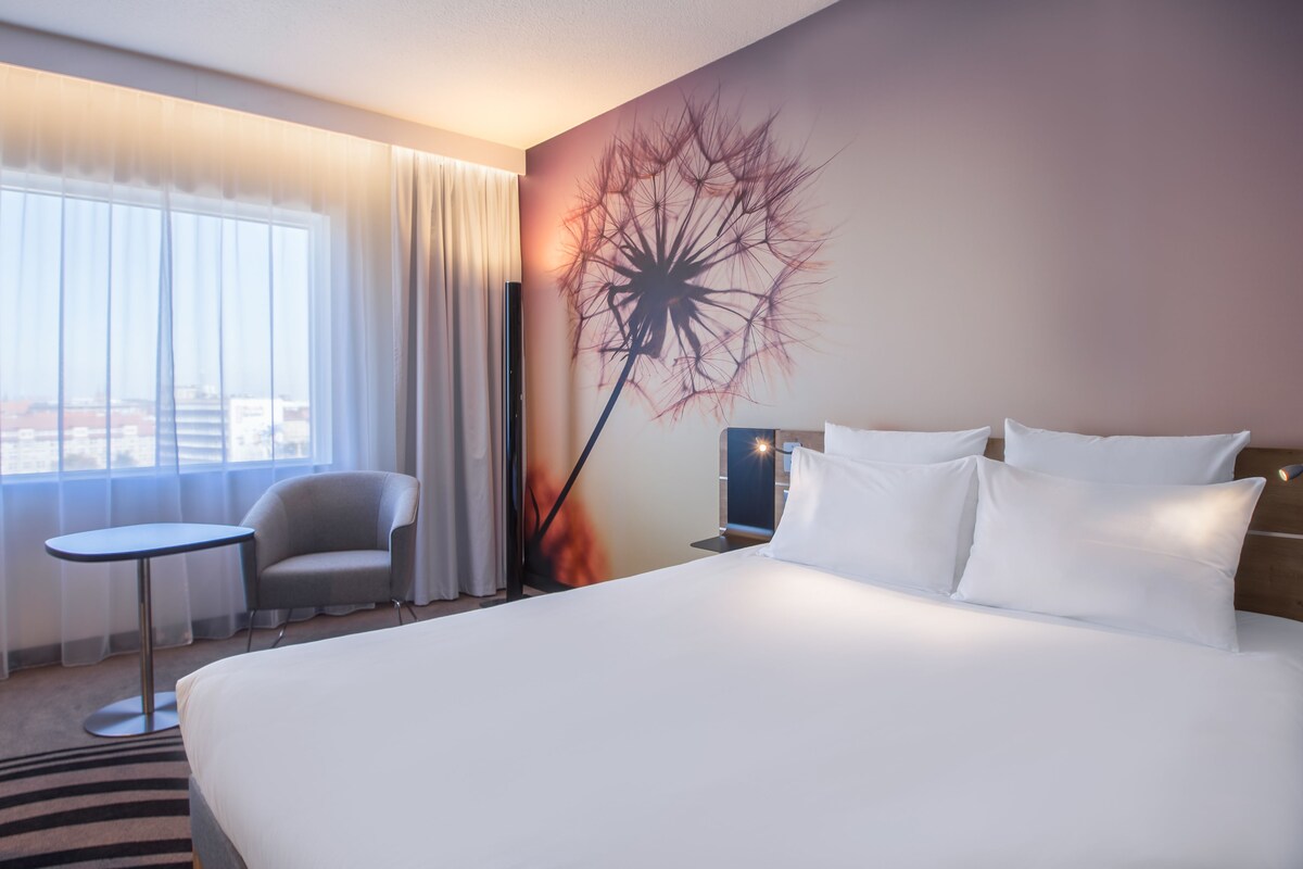 Una habitación de hotel con una cama grande, una mesita, una silla y un mural en la pared.