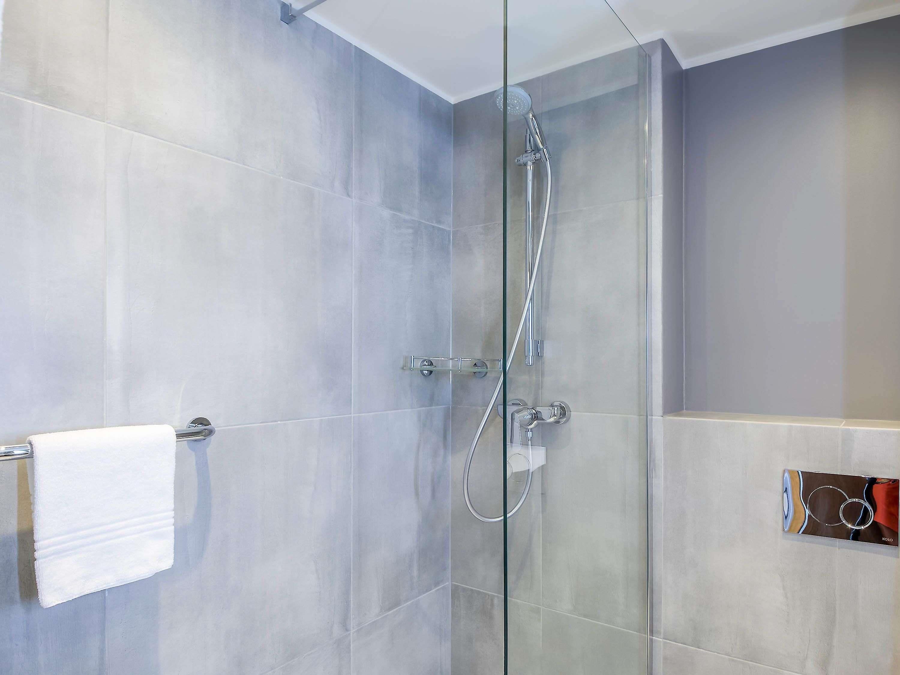 A modern shower with a glass door, a towel rack, and a wall-mounted control panel.