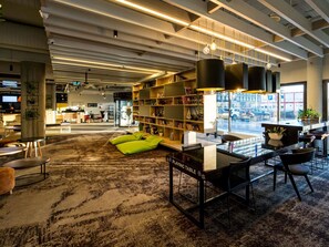 A modern interior with a reading area, bookshelves, and a view of the street. - Novotel Wroclaw Centrum (Wroclaw)