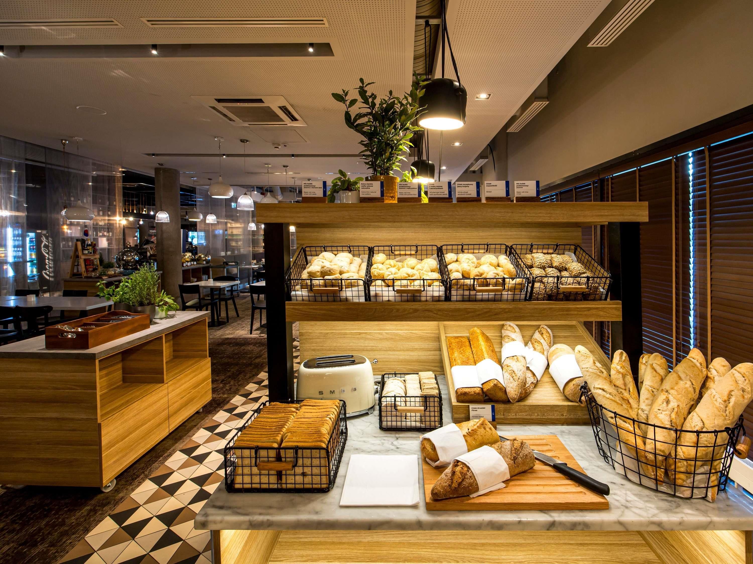 Mostrador de panadería con panes y pasteles variados, una máquina de café y una zona de estar con mesas y sillas.