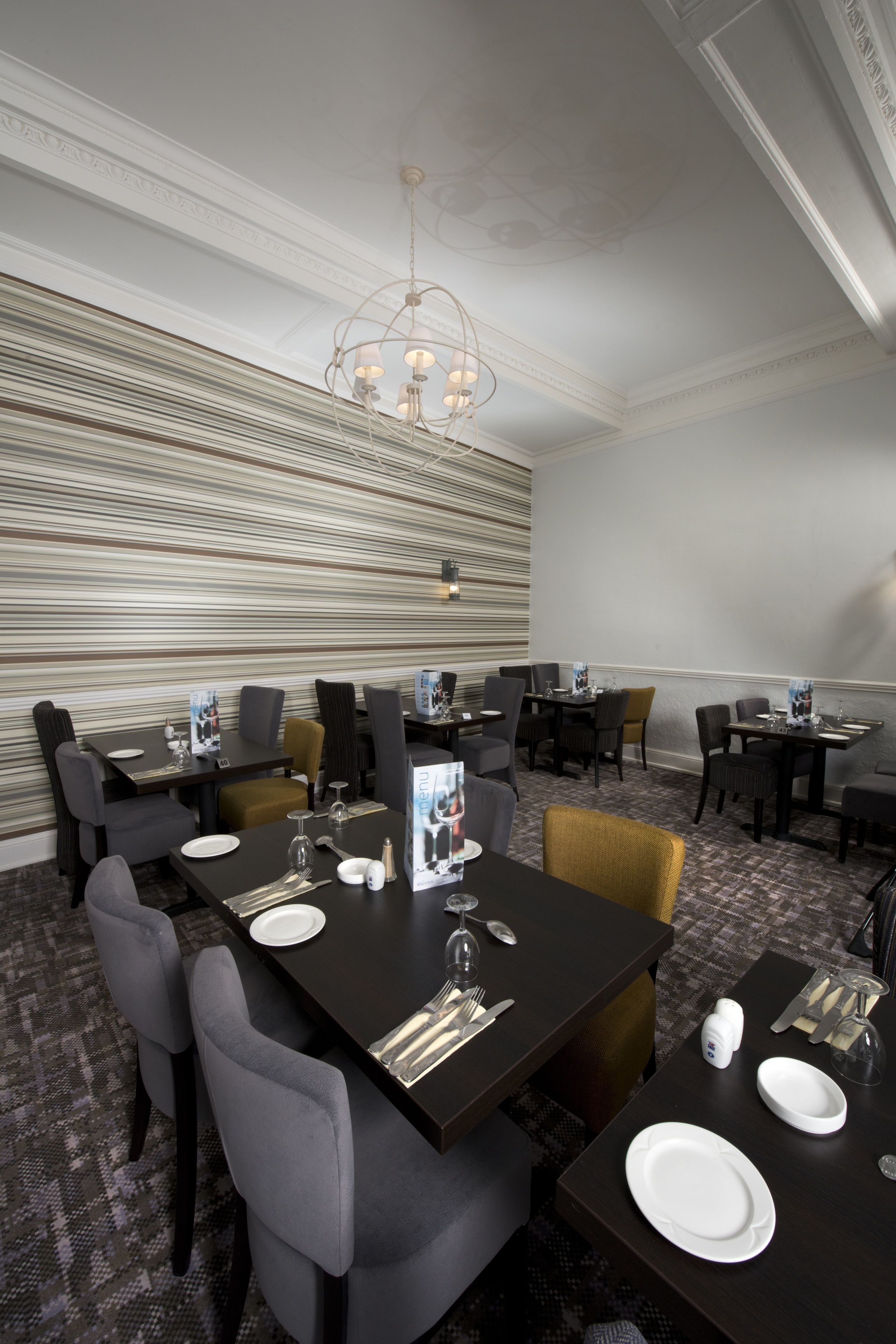 A conference room with dark wooden tables, grey upholstered chairs, and a patterned carpet.