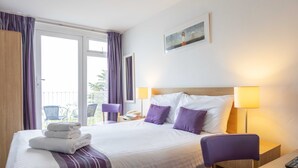 Una habitación de hotel con cama, una silla, escritorio y balcón con sillas.
