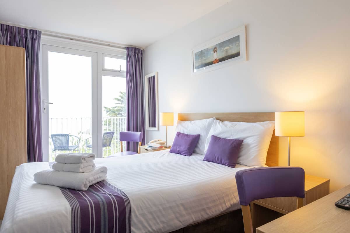 Una habitación de hotel con cama, una silla, escritorio y balcón con sillas.