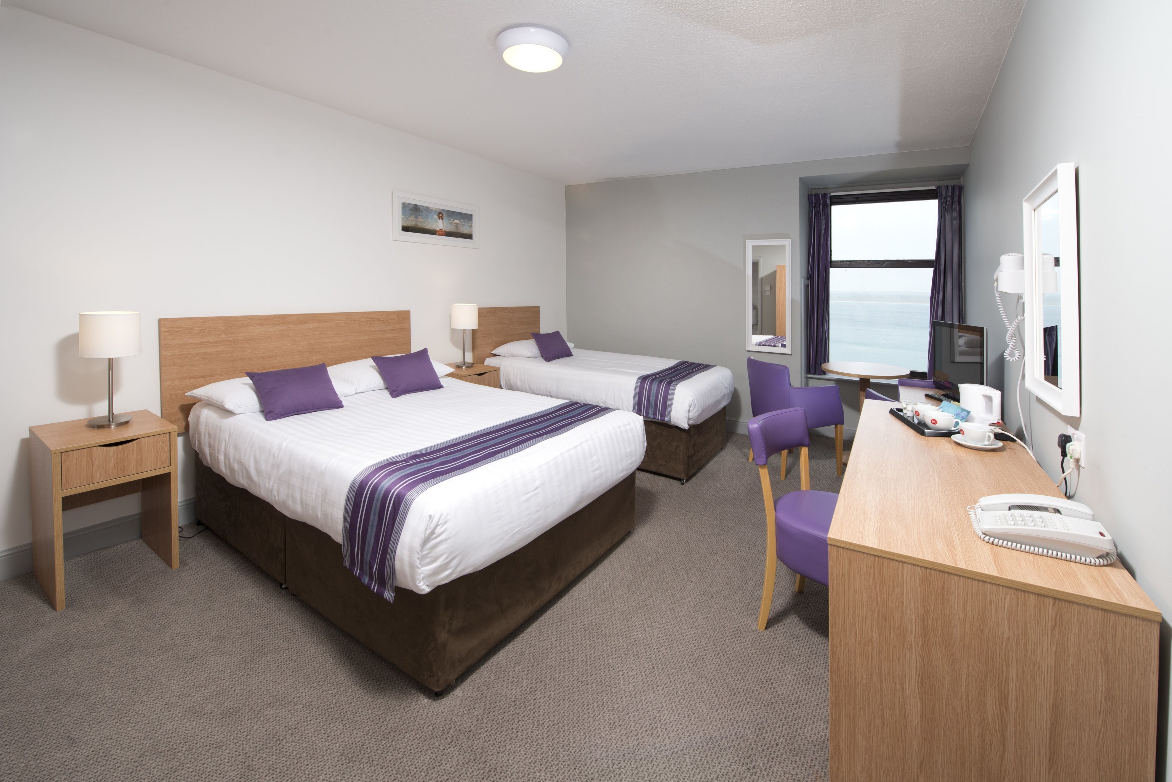 A hotel room with two beds, a desk, a chair, a lamp, a phone, and a window with a view.