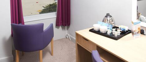 A room with a wooden desk, purple chairs, a window with curtains, and a view of the beach.