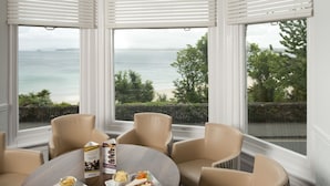 Un comedor con una mesa redonda, sillas color beige y vistas al mar a través de amplios ventanales.