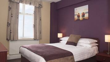 A hotel room with a large bed, two bedside lamps, a window with curtains, and a painting on the wall.