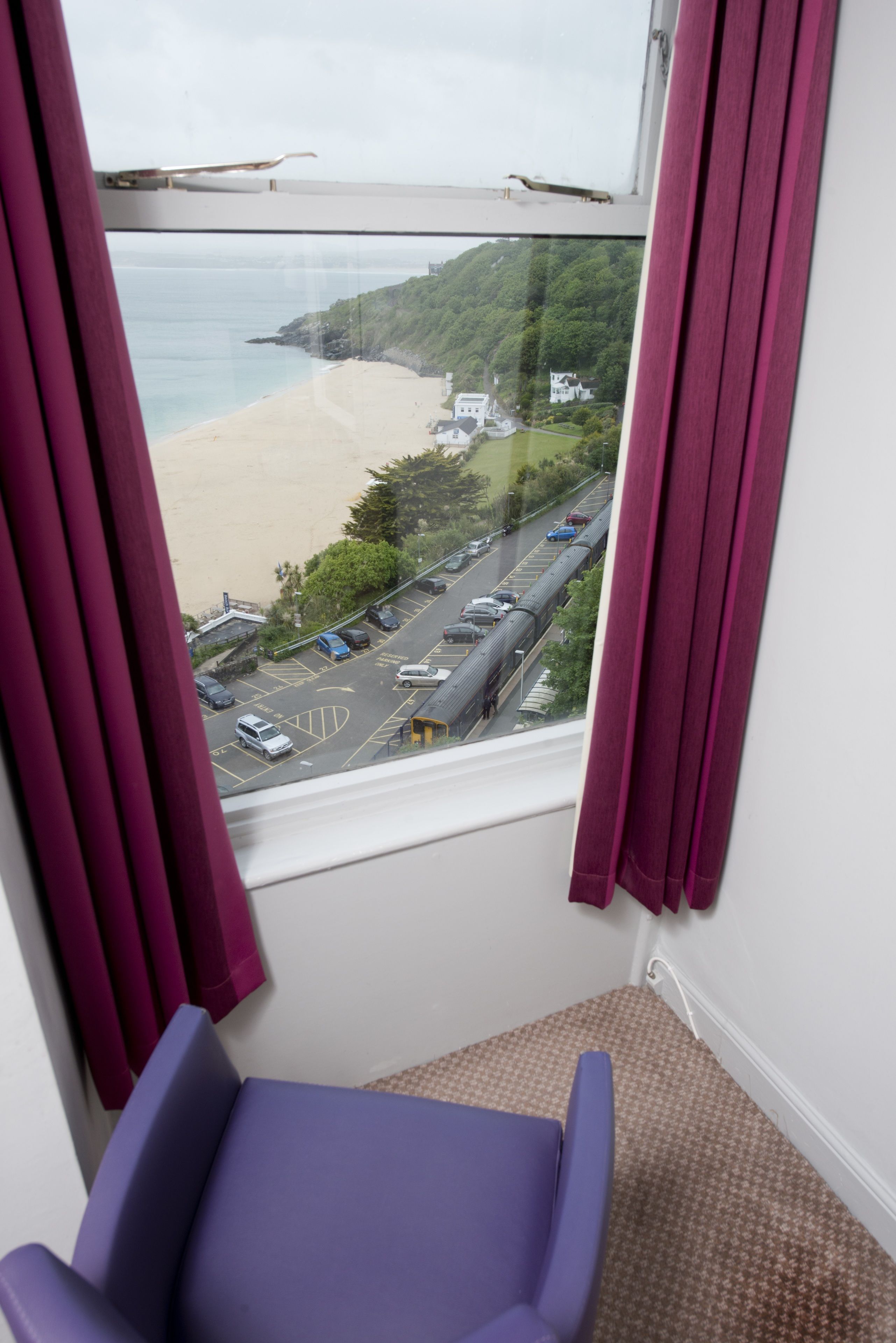 A room with a window overlooking a beach and a parking lot.