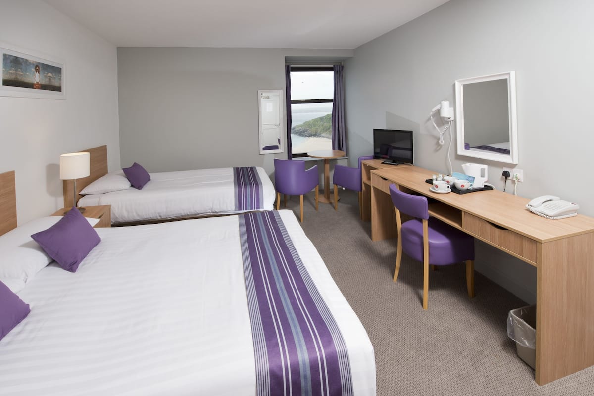 Habitación de hotel con dos camas, un escritorio, sillas, televisión y ventana con vistas.