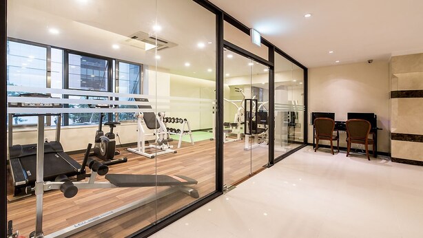 A modern gym with exercise equipment, a weight bench, and a glass wall offering a view of the city. - Korea Tourist Hotel (Suwon)
