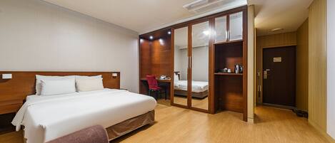 A hotel room with a large bed, a desk with a chair, a wardrobe, and a door.