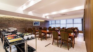 A conference room with multiple tables and chairs, a buffet area with various food items, and a brick wall with a painting. - Korea Tourist Hotel (Suwon)