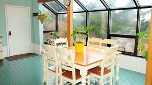 A dining area with a wooden table and white chairs, a yellow pot on the table, and a clock on the wall. - Cranky Crow Bed and Breakfast (Kodiak)
