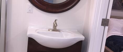 A bathroom with a round mirror, a white sink, and dark brown cabinets.