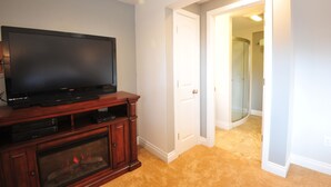 A room with a flat-screen TV on a wooden entertainment center, a white door, and a hallway leading to a bathroom. - Cranky Crow Bed and Breakfast (Kodiak)