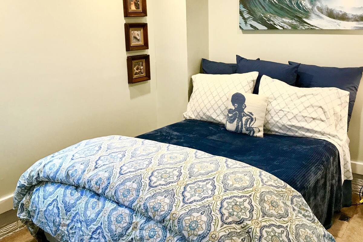A bedroom with a bed, pillows, a wall-mounted picture, and a large painting.
