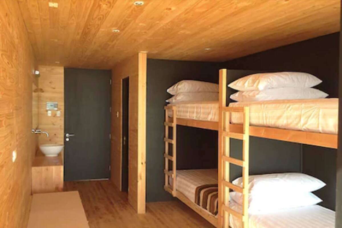 Una habitación compacta de estilo cabaña, con literas, un lavabo y una puerta que da a otra habitación.