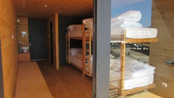 Interior de madera con literas, un baño pequeño y vista a un paisaje nevado a través de una ventana.