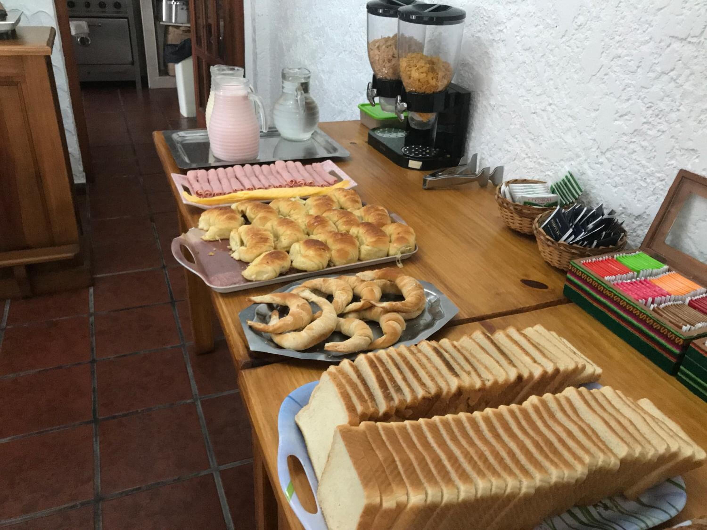 A kitchen area with various baked goods, including bread rolls, croissants, and pastries, displayed on trays and plates.