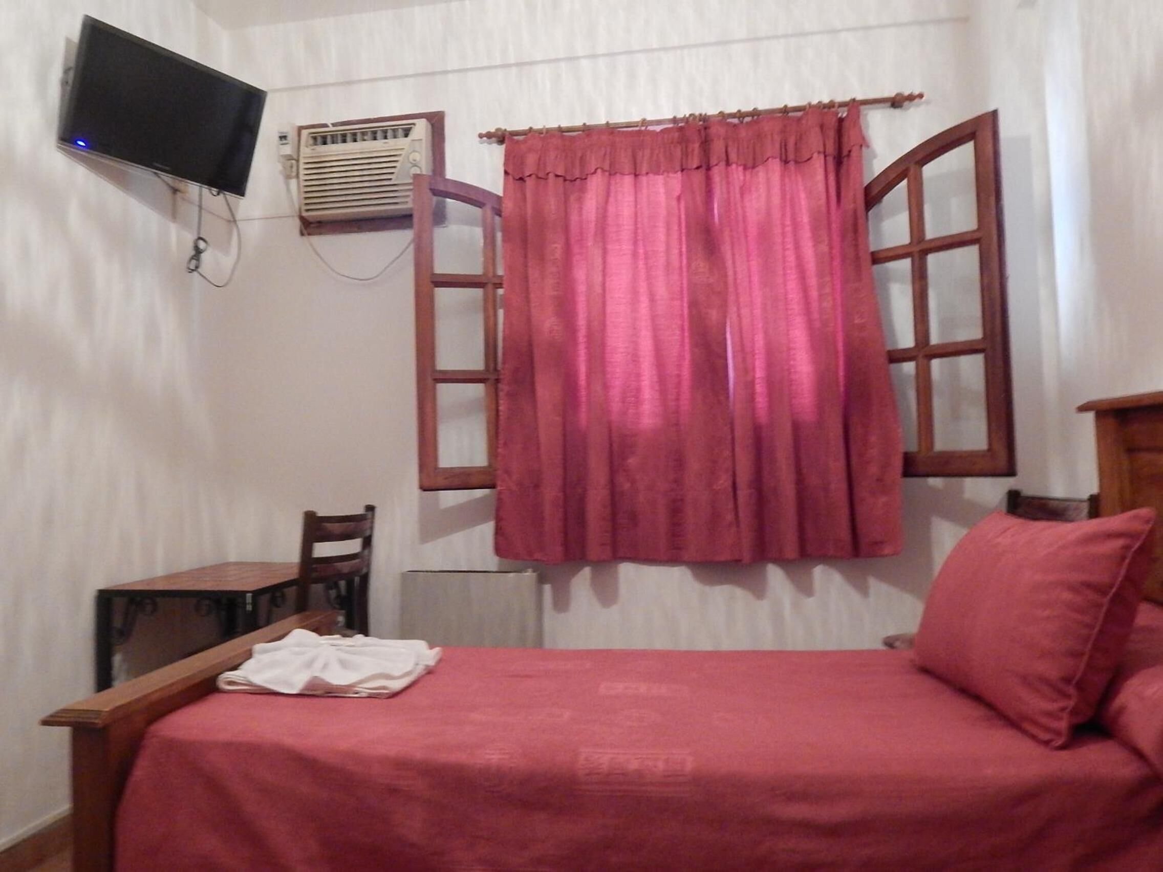 Ein Schlafzimmer mit einem Bett, einem an der Wand montierten Fernseher, einer Klimaanlage und einem Fenster mit Vorhängen.