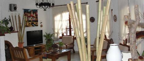 A living room with a TV, wooden furniture, bamboo decorations, and a chandelier.