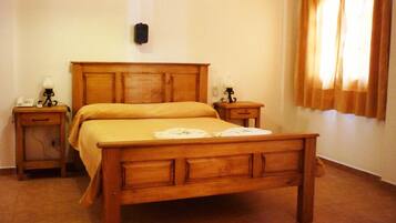 A wooden bed with a headboard, two bedside tables with lamps, and a window with curtains.