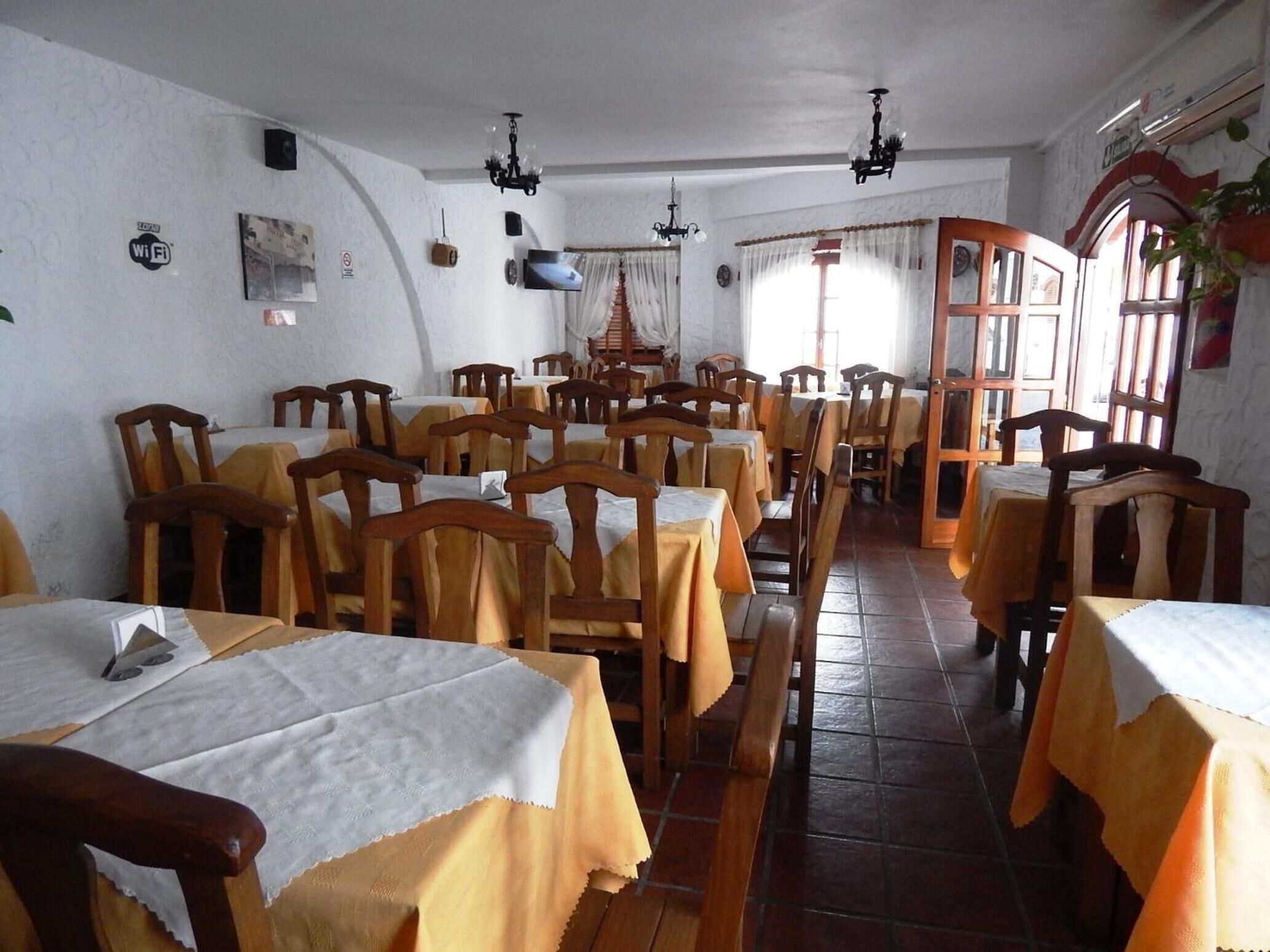 Comedor con mesas y sillas de madera, un candelabro y una pantalla de televisión.