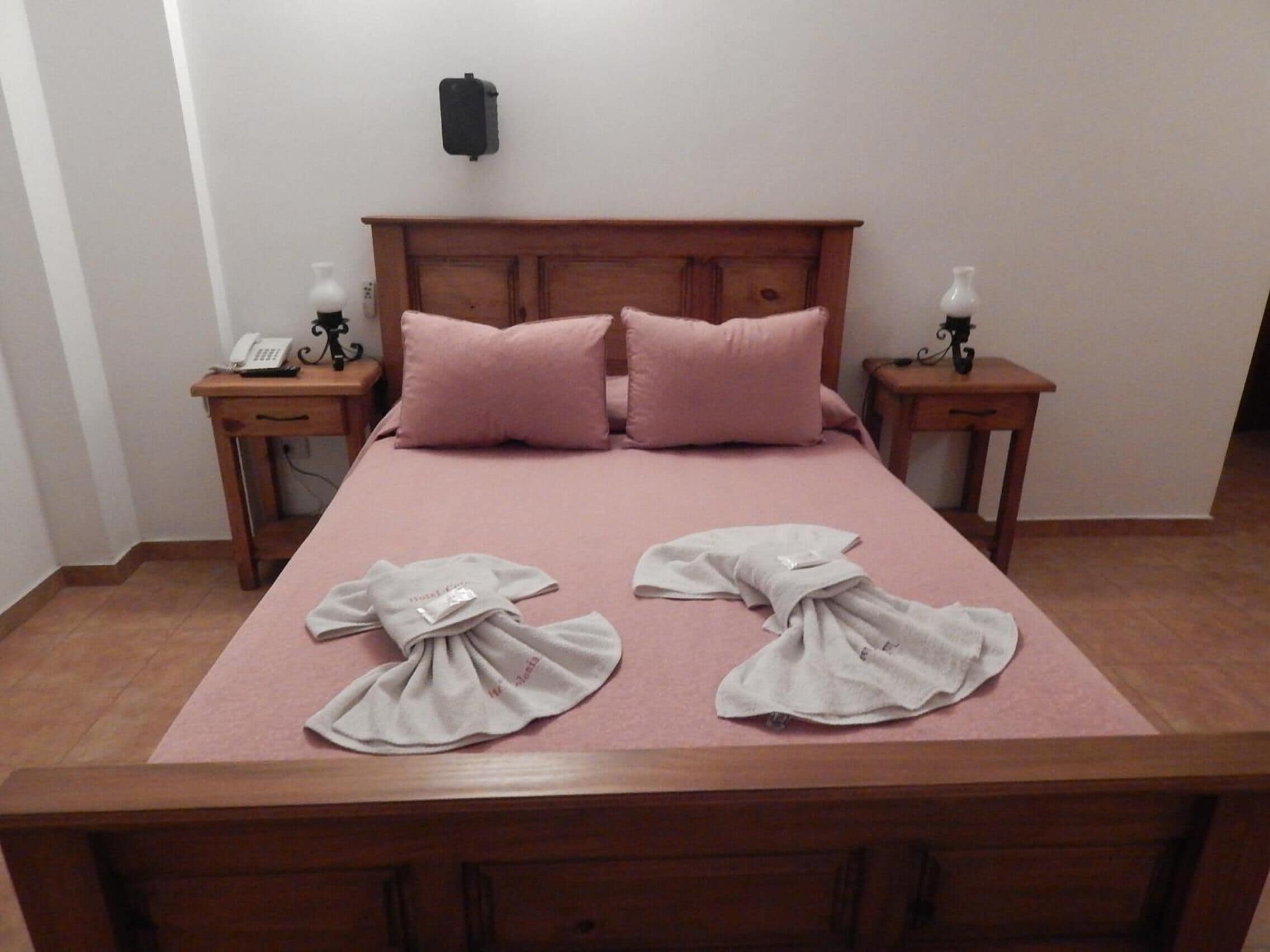 Un lit bien fait, avec une literie rose et deux serviettes pliées posées sur le lit.