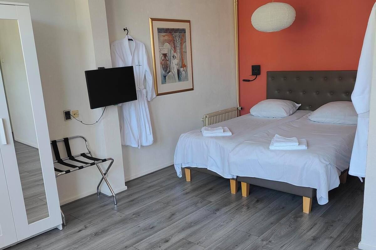 A hotel room with a bed, a desk, a chair, a television, and a painting on the wall.