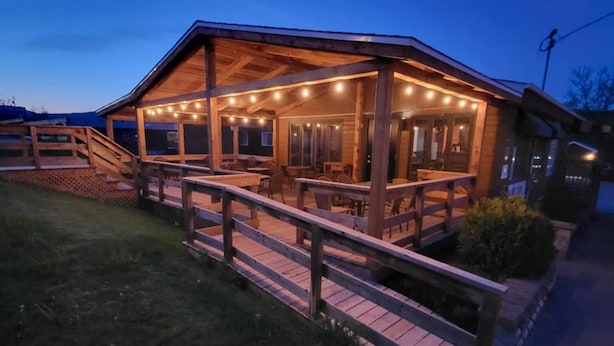 A wooden building with a covered patio area, outdoor seating, and a wooden fence.